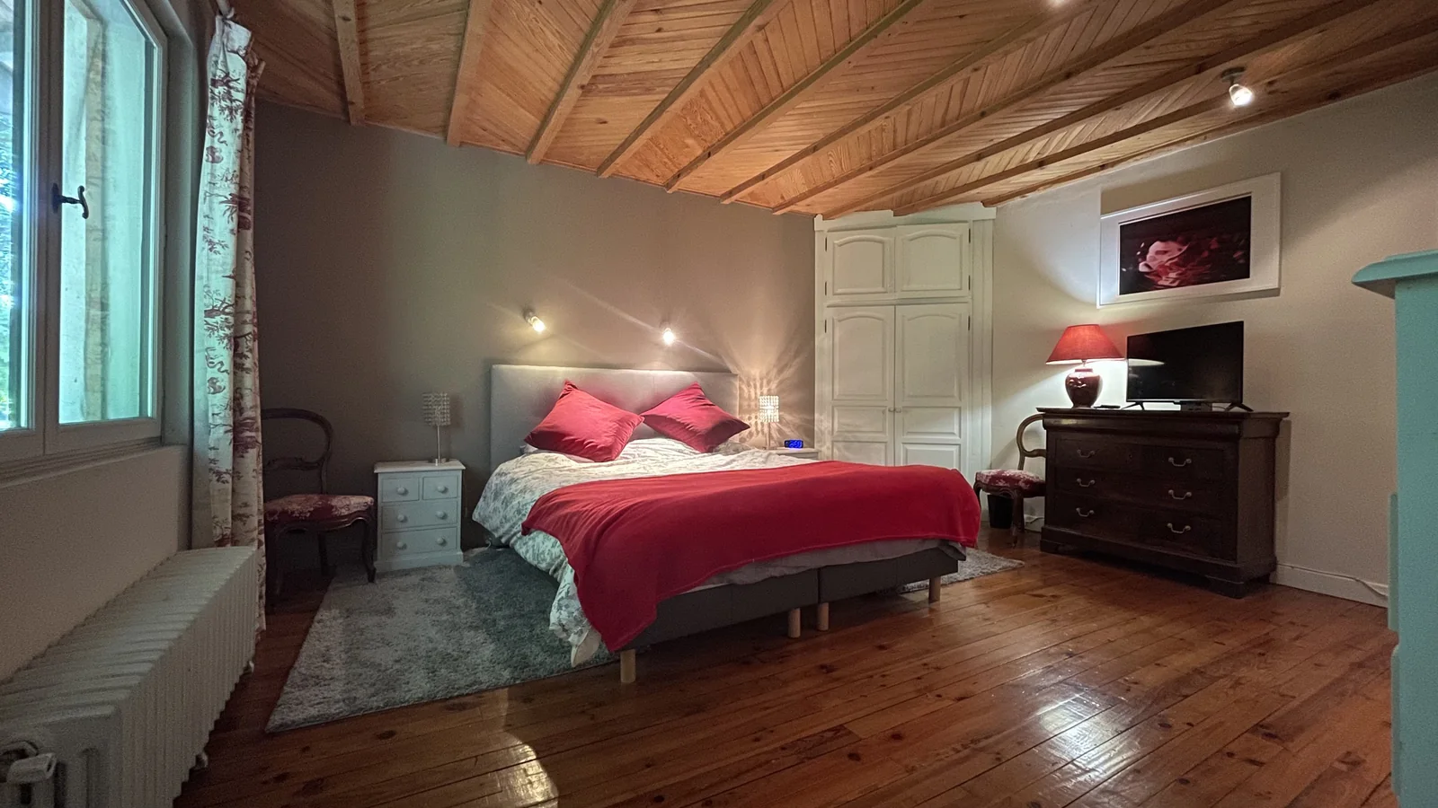 La chambre rouge avec grand lit, parquet et plafond en bois
